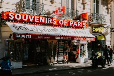Street view of a Paris souvenir shop with motorbikes, showcasing signage and storefront items. Vue de rue d'une boutique de souvenirs parisienne avec des motos, mettant en avant les panneaux et les articles de devanture.