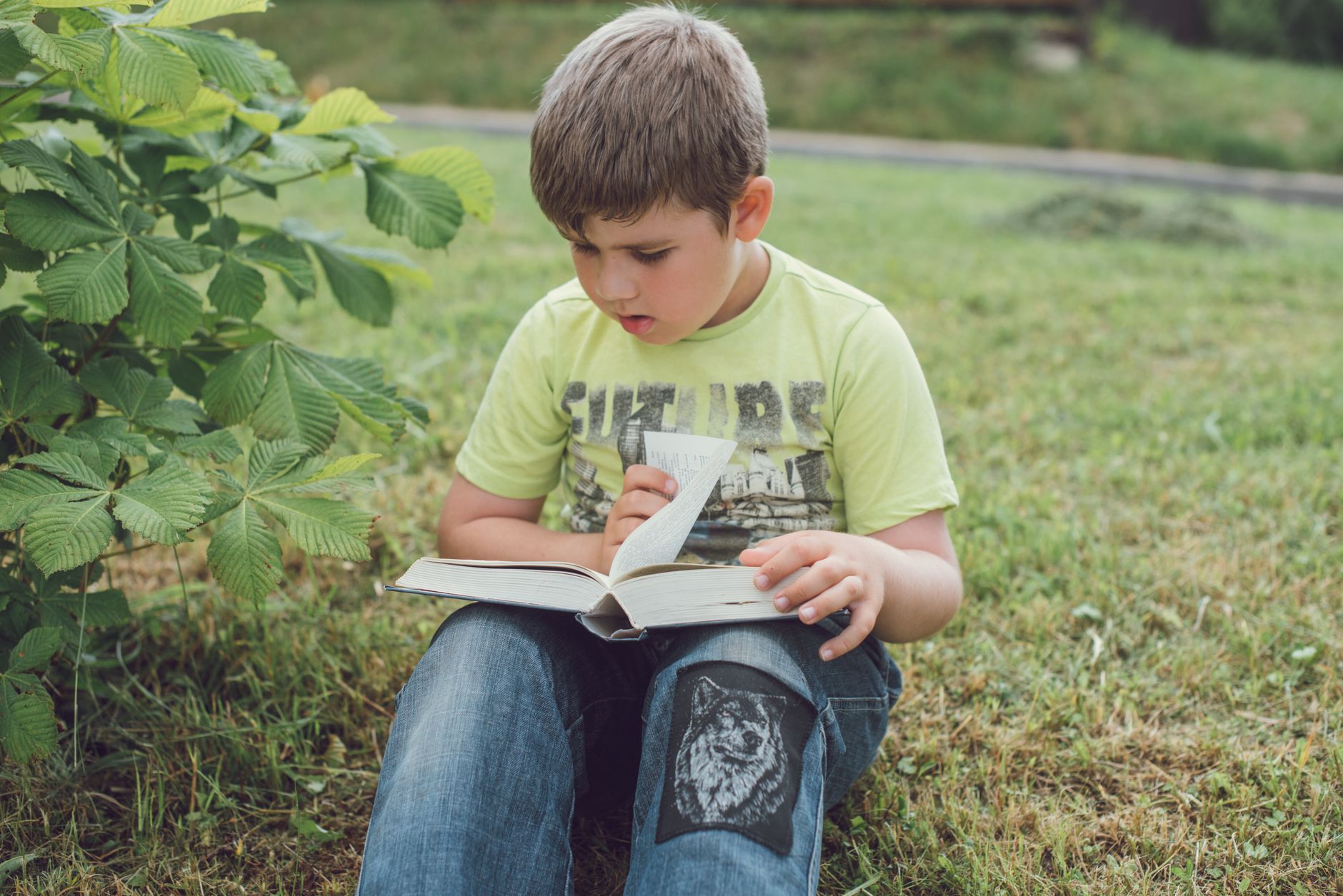 Jeune garçon allongé dans l'herbe en train de lire